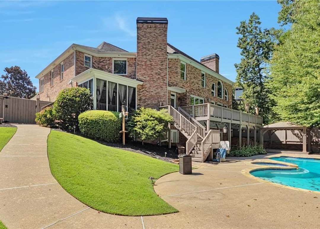 Rear elevation of 1421 Castlebrooke Way showing the full four-sided brick facade, two brick chimneys, a raised wood deck, and the pool patio at right