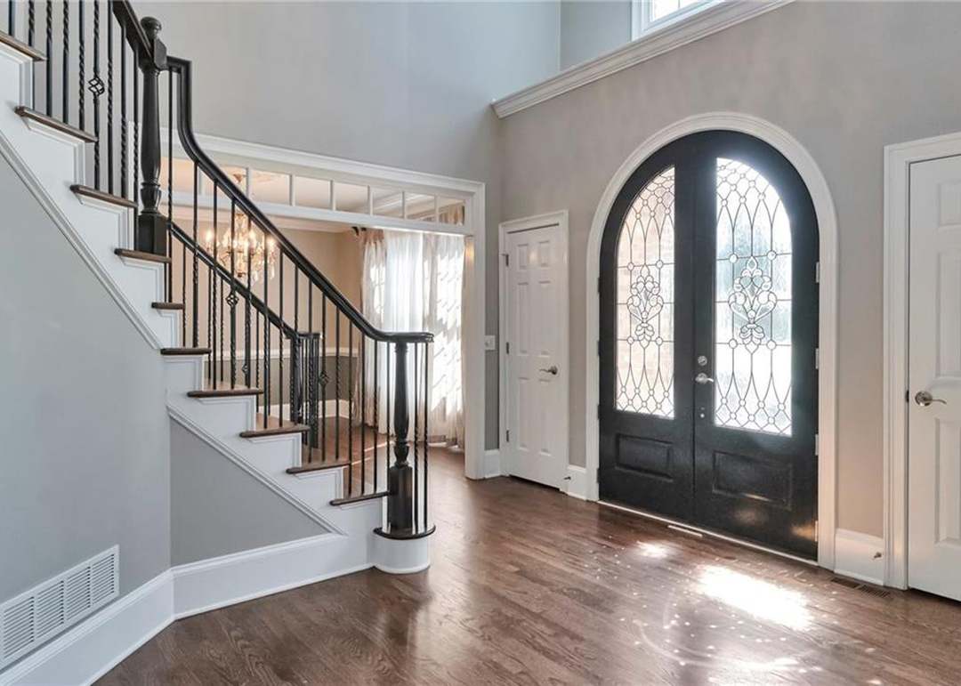 Two-story entry foyer of 1421 Castlebrooke Way with a curved iron-baluster staircase, an arched leaded-glass front door, and hardwood floors