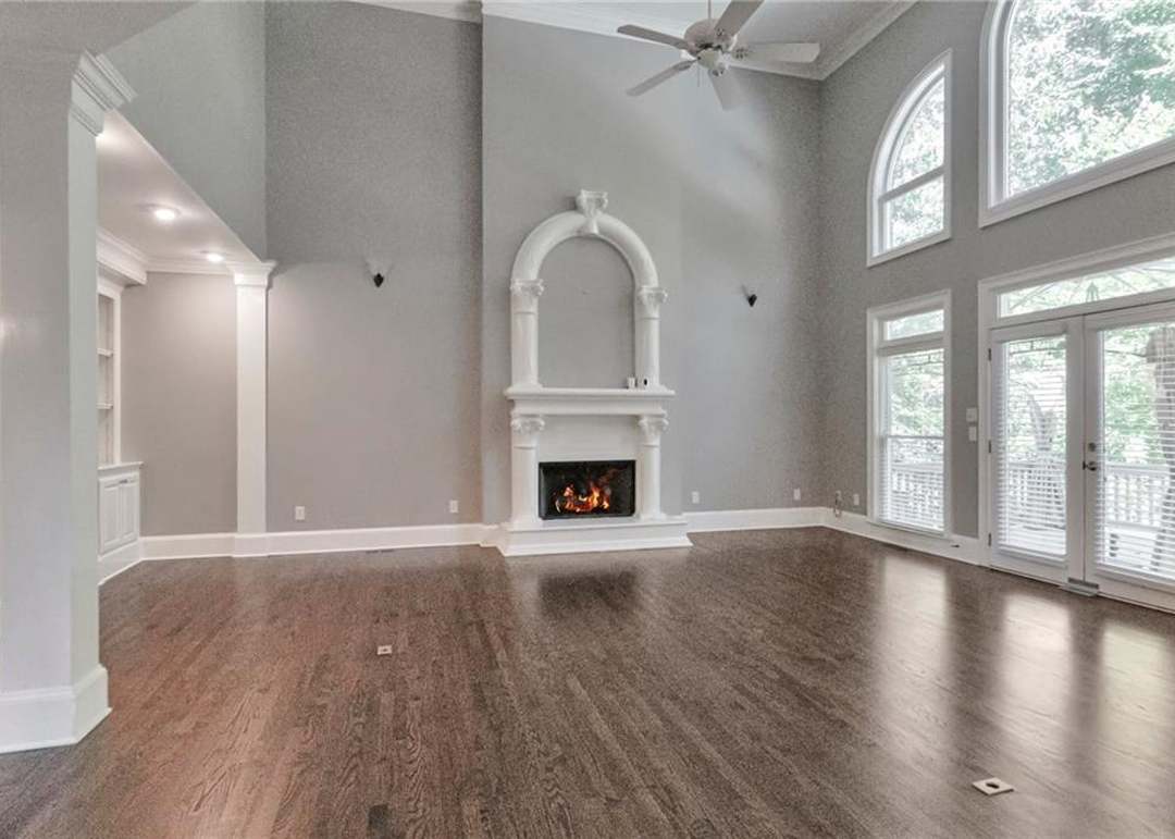 Two-story great room with a white arched fireplace surround holding a lit fire, a wall of tall arched windows, and French doors to the rear deck