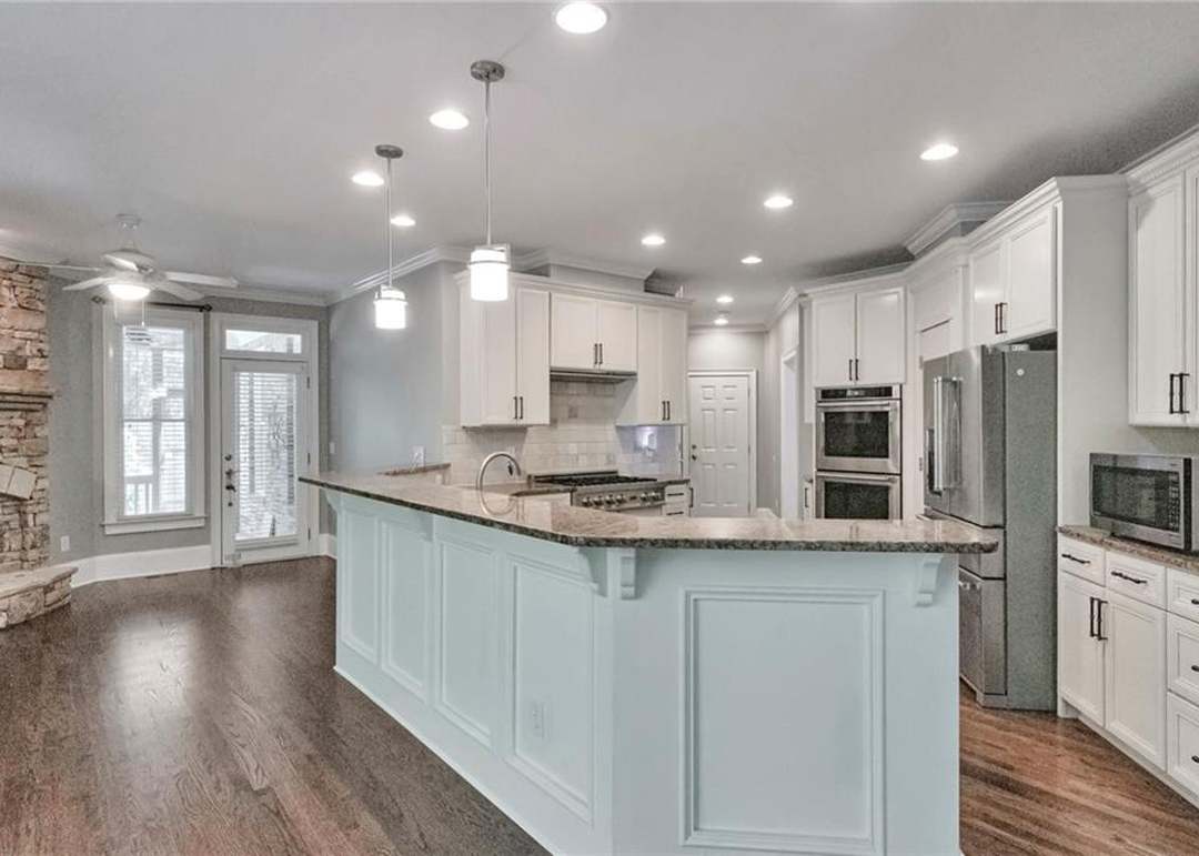 Kitchen island and peninsula with granite tops and pendant lights, opening to a keeping room with a stacked-stone fireplace