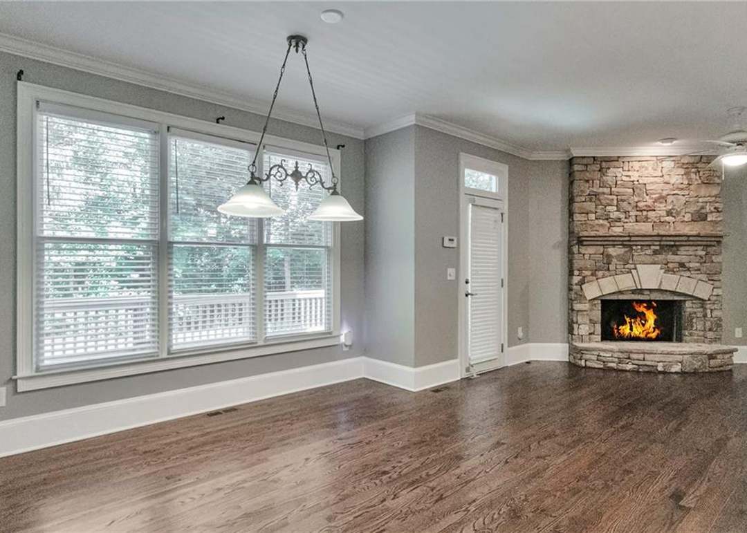 Keeping room with a floor-to-ceiling stacked-stone corner fireplace holding a lit fire, a window wall, and a door to the deck