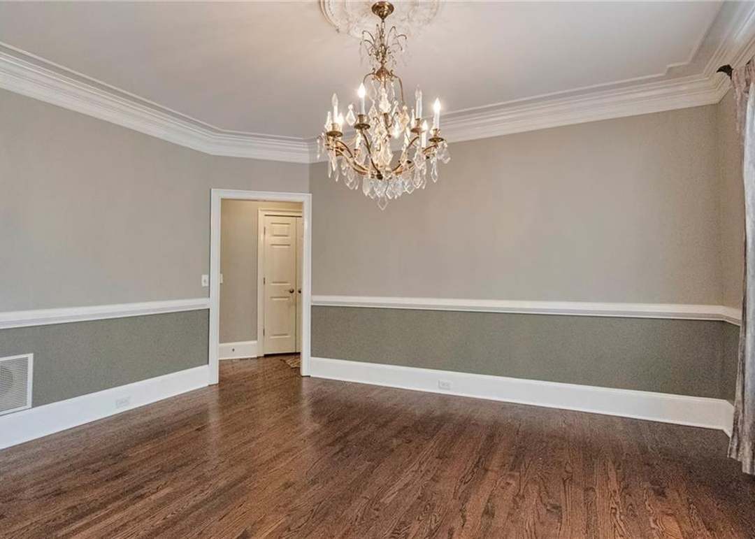 Formal dining room with a crystal chandelier, two-tone walls with chair-rail wainscoting, and hardwood floors