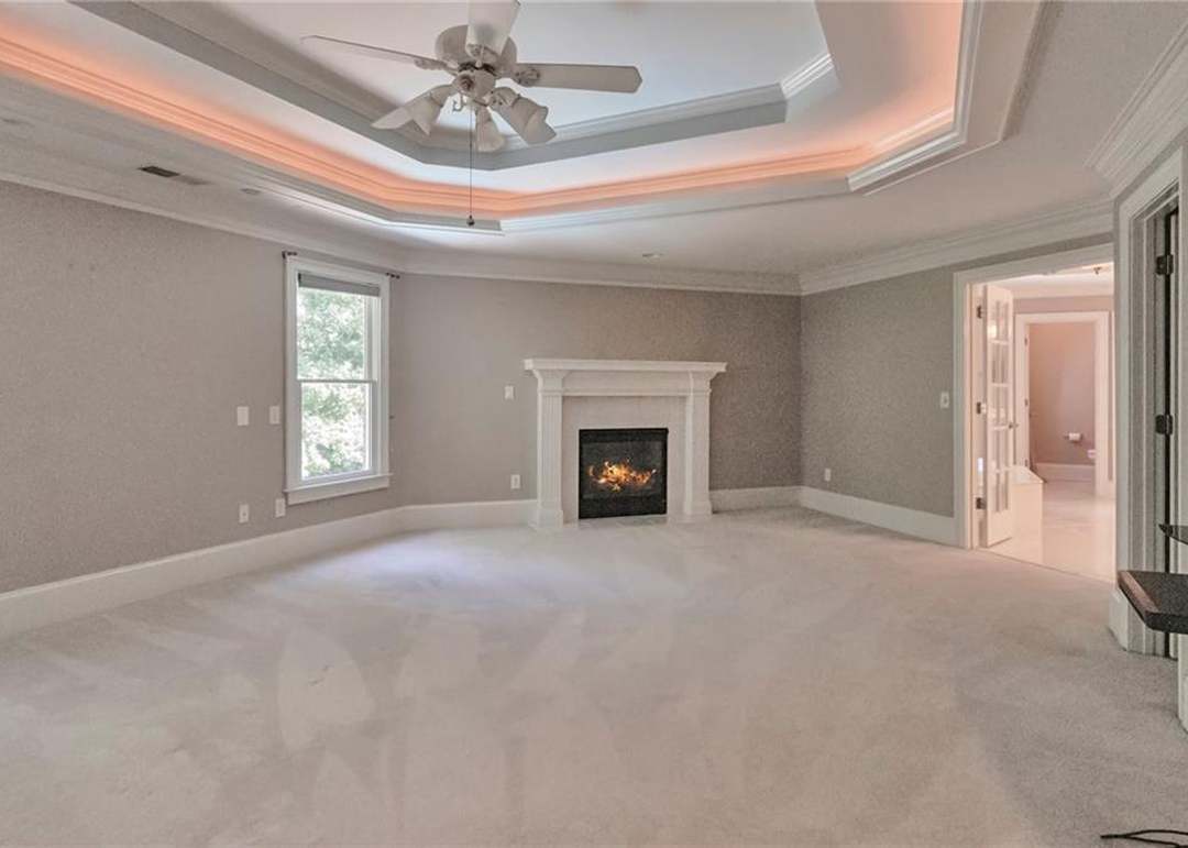 Owner's retreat with an octagonal trey ceiling lit by cove lighting, a marble fireplace holding a lit fire, and a private sitting area