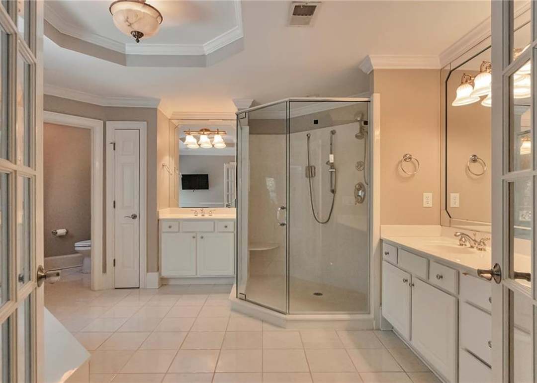 Owner's spa bath with dual white vanities, a large frameless glass corner shower, tile flooring, and a trey ceiling