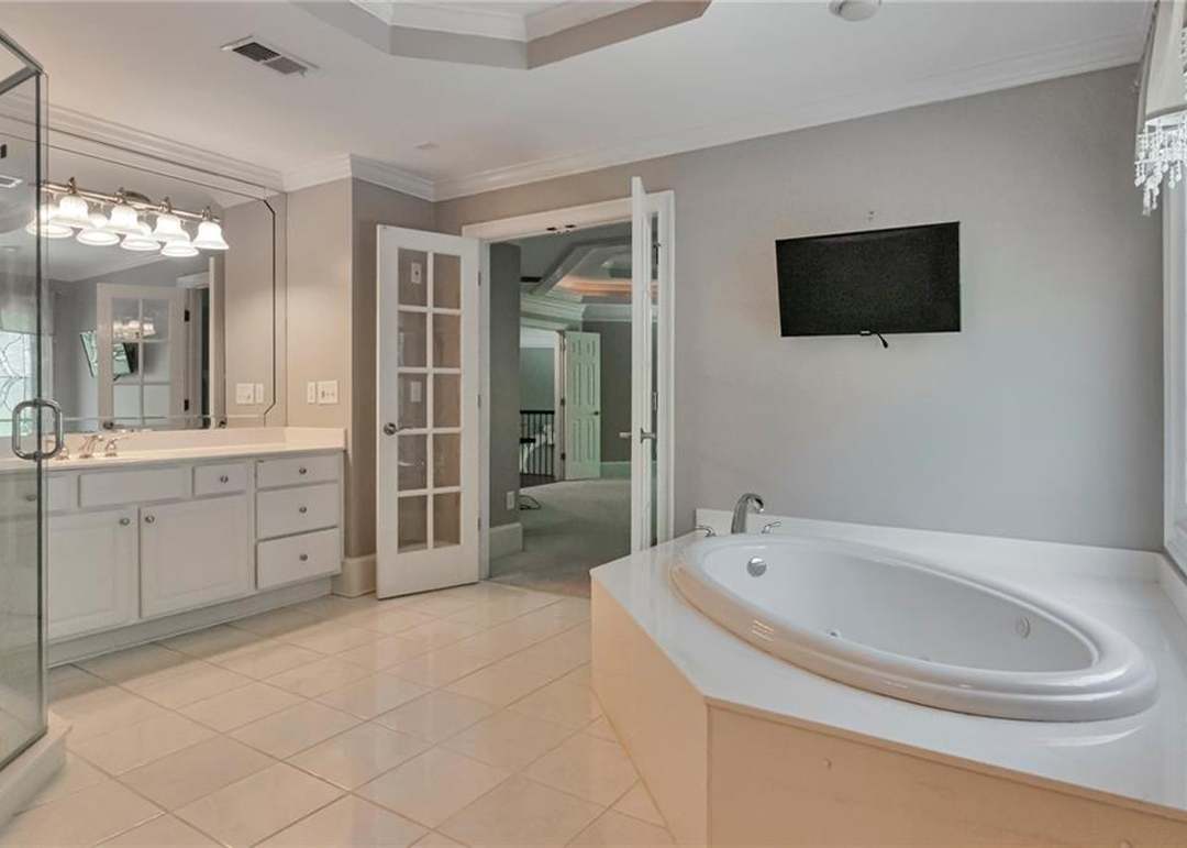 Owner's bath with a jetted corner soaking tub, French doors back to the bedroom, and a second white vanity