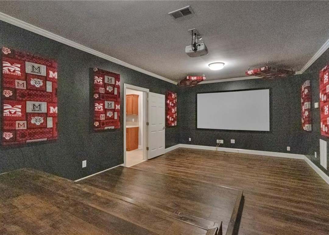 Finished basement home theater with a ceiling-mounted projector, a large drop-down screen, a stepped riser, and dark walls