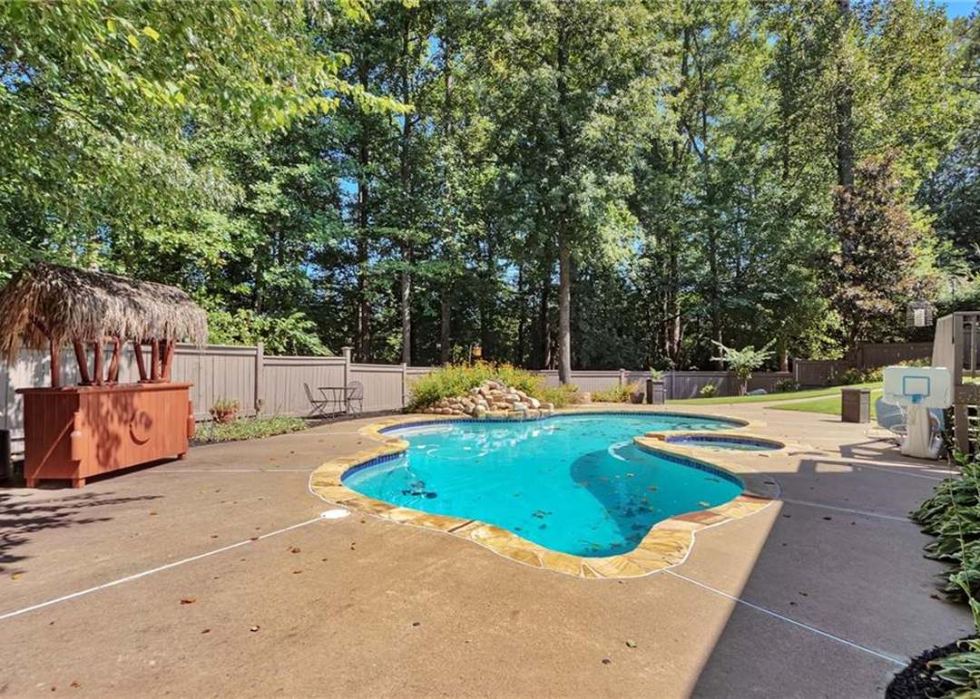 Freeform pebble-bottom pool with a raised spillover spa, flagstone coping, a tiki cabana, and a wooded privacy backdrop