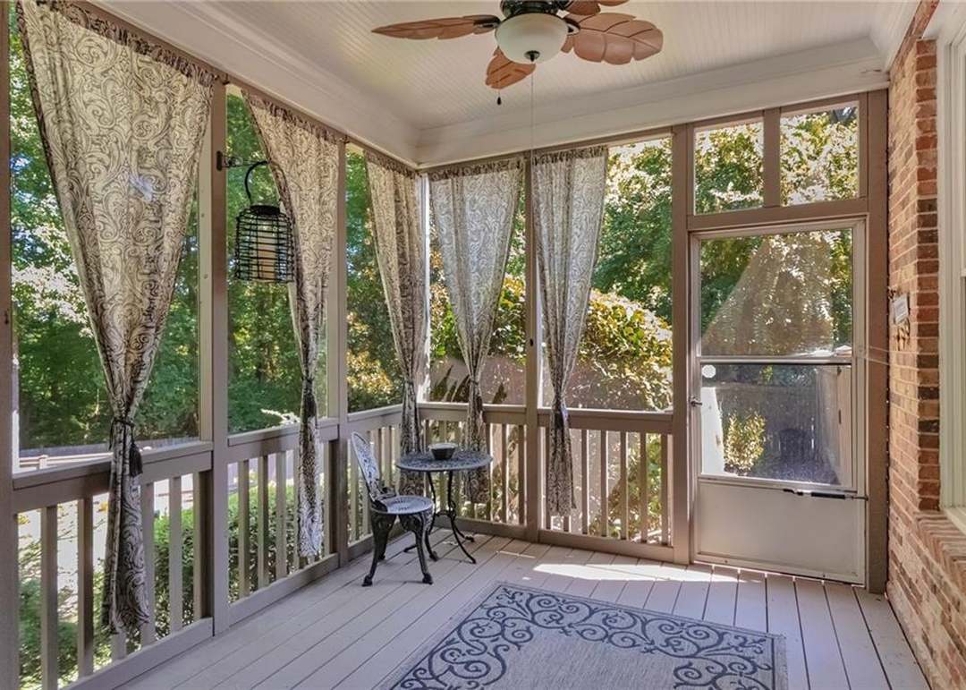 Screened porch with a beadboard ceiling, a ceiling fan, patterned drapes, and a bistro set overlooking the wooded backyard